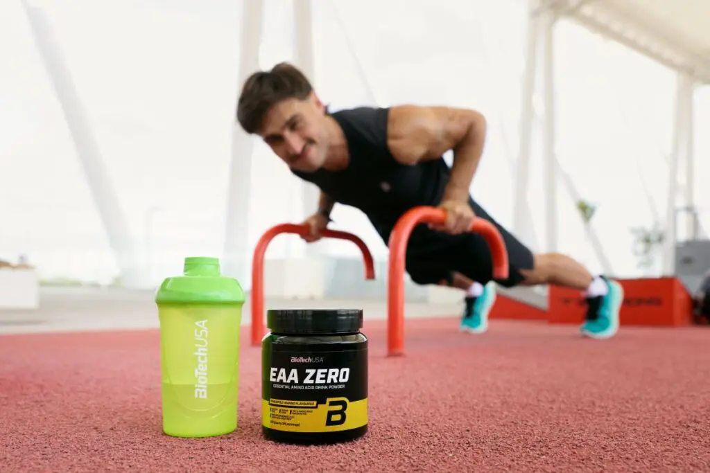 Un sportif en salle de musculation tenant un shaker de compléments en acides aminés, illustrant l'importance de la supplémentation pour la performance.